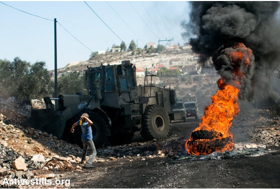 A demonstrator hurls a stone at an Israeli army bulldozer during the weekly demonstration against the occupation in the West Bank village of Kafr Qaddum, October 25, 2013.