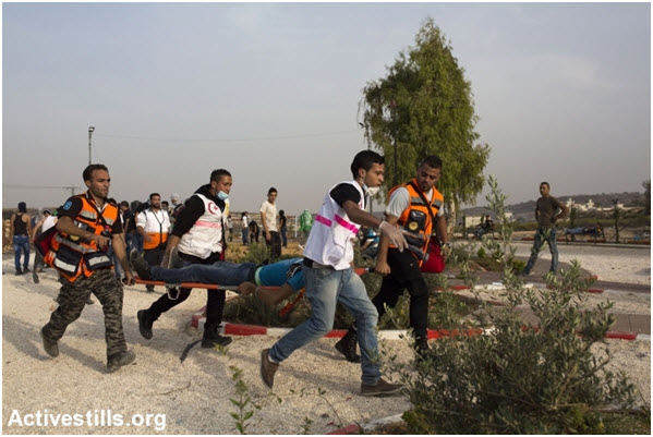 Palestinian medics carry an injured protester during a clash with Israeli forces near the settlement of Beit-El, the West-Bank, on October 12, 2015.