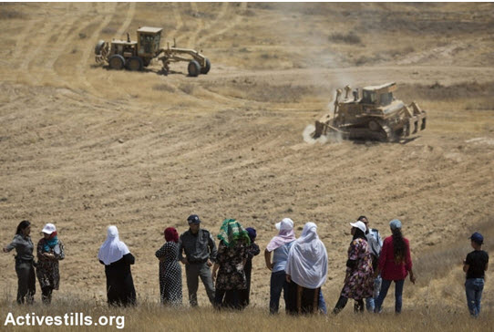 Arab-Bedouin women, supervised by Israeli polic officers, can only helplessly look on as bulldozers of the Jewish National Fund (JNF) plow up private lands belonging to the unrecognized village of Al-Araqib, in preparation for the planting of a JNF forest, July 20, 2016. During the last six years, Al-Araqib has been demolished more than one hundred times.