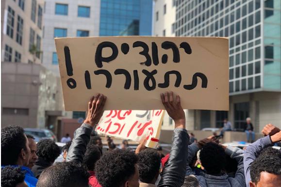 2,000 asylum seekers and Israeli activists gathered on Monday, January 22, outside of the Rwandan embassy in Herzliya to protest the reported agreement between the governments of Israel and Rewanda to deport asylum seekers to the latter country. The raised placard reads "Jews, wake up!"
