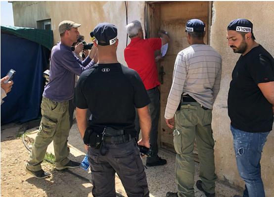 An Israeli official accompanied by armed police pins an eviction order on the front door of a home in the Arab-Bedouin village of Umm al-Hiran in the Negev.
