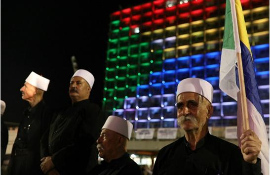 Elder religious leaders of the Druze community in Israel during the mass protest last Saturday night, August 4, at Rabin Square; in the background, the building of Tel Aviv’s municipality is lit up with the colors of the Druze flag.
