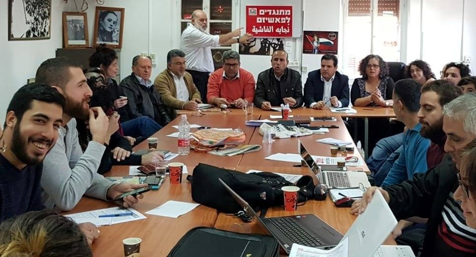 Hadash electoral committee meeting last weekend to launch the party's campaign for the upcoming general elections for the 21st Knesset; the red placard held up in the background reads "Opposing Fascism."