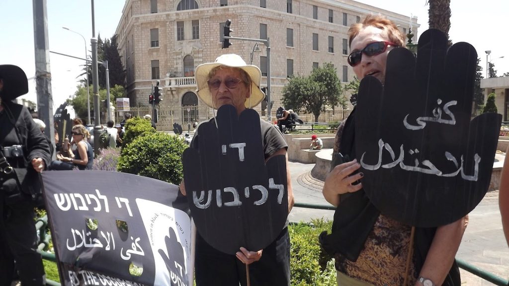 Women in Black holding a Friday protest vigil at Paris Square in central West Jerusalem, near the official residence of the Prime Minister; the black placards in the shape of a stop sign read "End the Occupation" in Arabic and Hebrew.