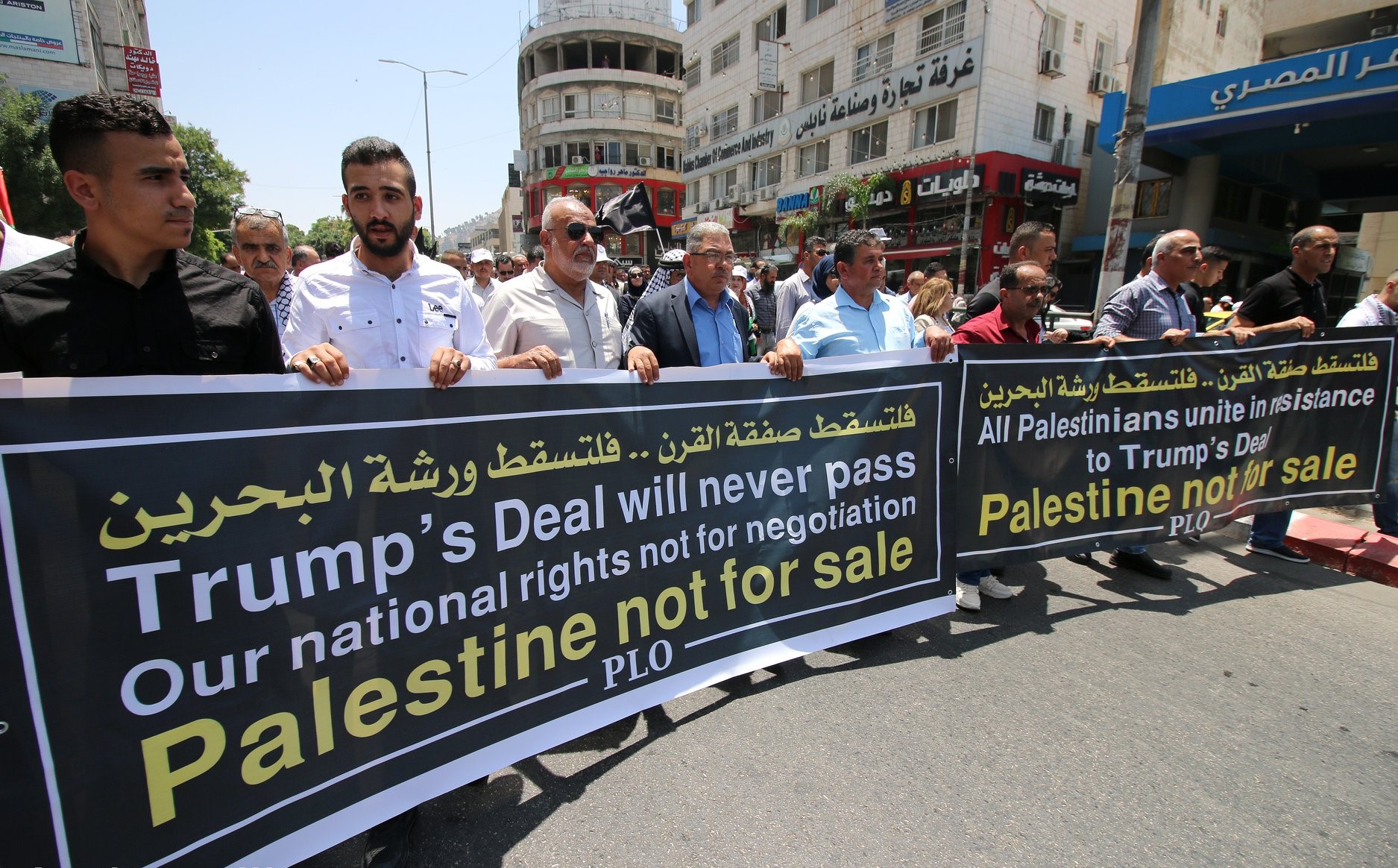 Palestinians demonstrate in Ramallah in late June 2019 during the then ongoing "Peace to Prosperity" workshop, initiated by the Trump administration, taking place in Bahrain. The slogan in Arabic at the top of the banners reads: "Down with the Deal of the Century.. Down with the Bahrain Workshop."