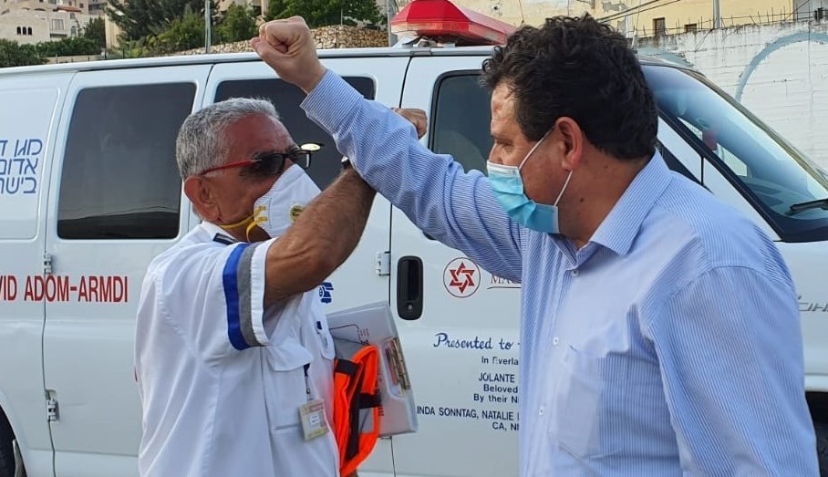 Joint List chairman, MK Ayman Odeh (Hadash) and a paramedic greet one another in the village of Bi'ina village in the Galilee, Monday, April 13.