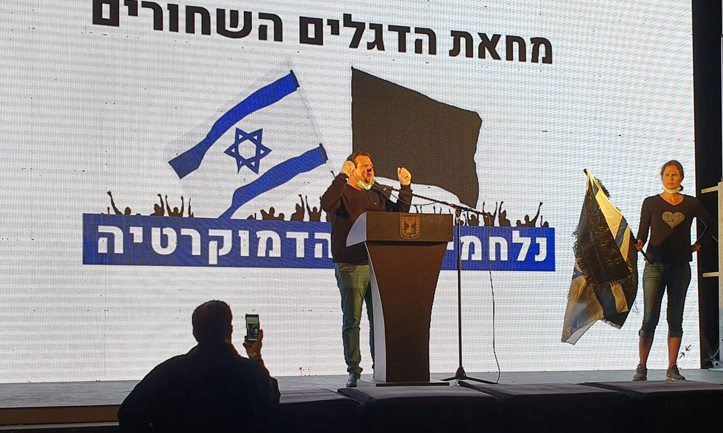 MK Ayman Odeh addresses protesters in the rally held Sunday evening in Central Tel-Aviv. The backdrop behind him reads: "Black Flag Protest – Fighting for Democracy."