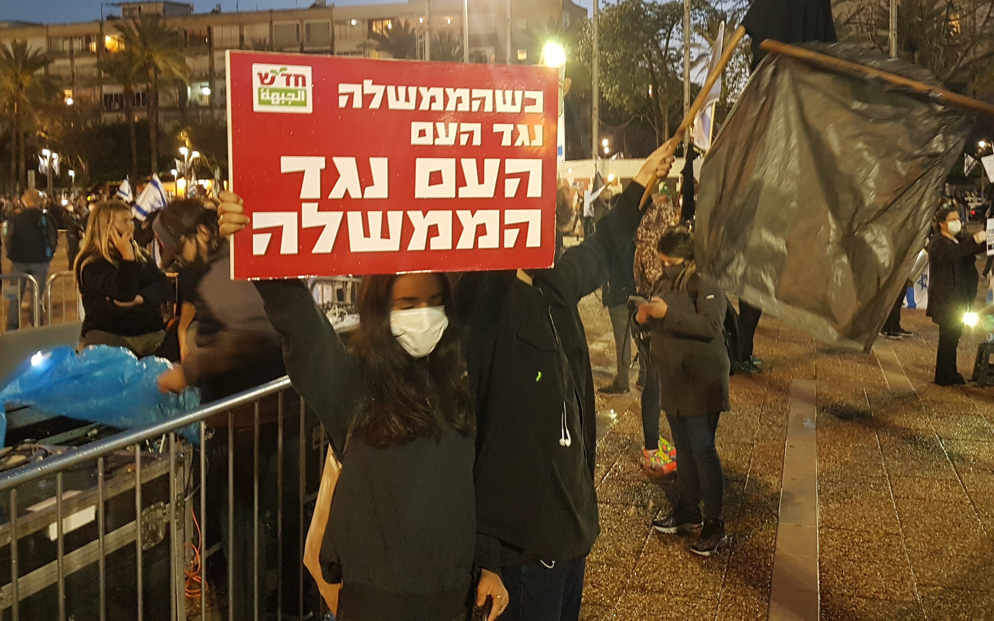 Two of the Hadash activists who participated in the demonstration organized by the Black Flag Movement on Saturday evening, April 25, Tel Aviv's Rabin Square; the Hadash placard reads "When the government is against the people, the people are against the government."