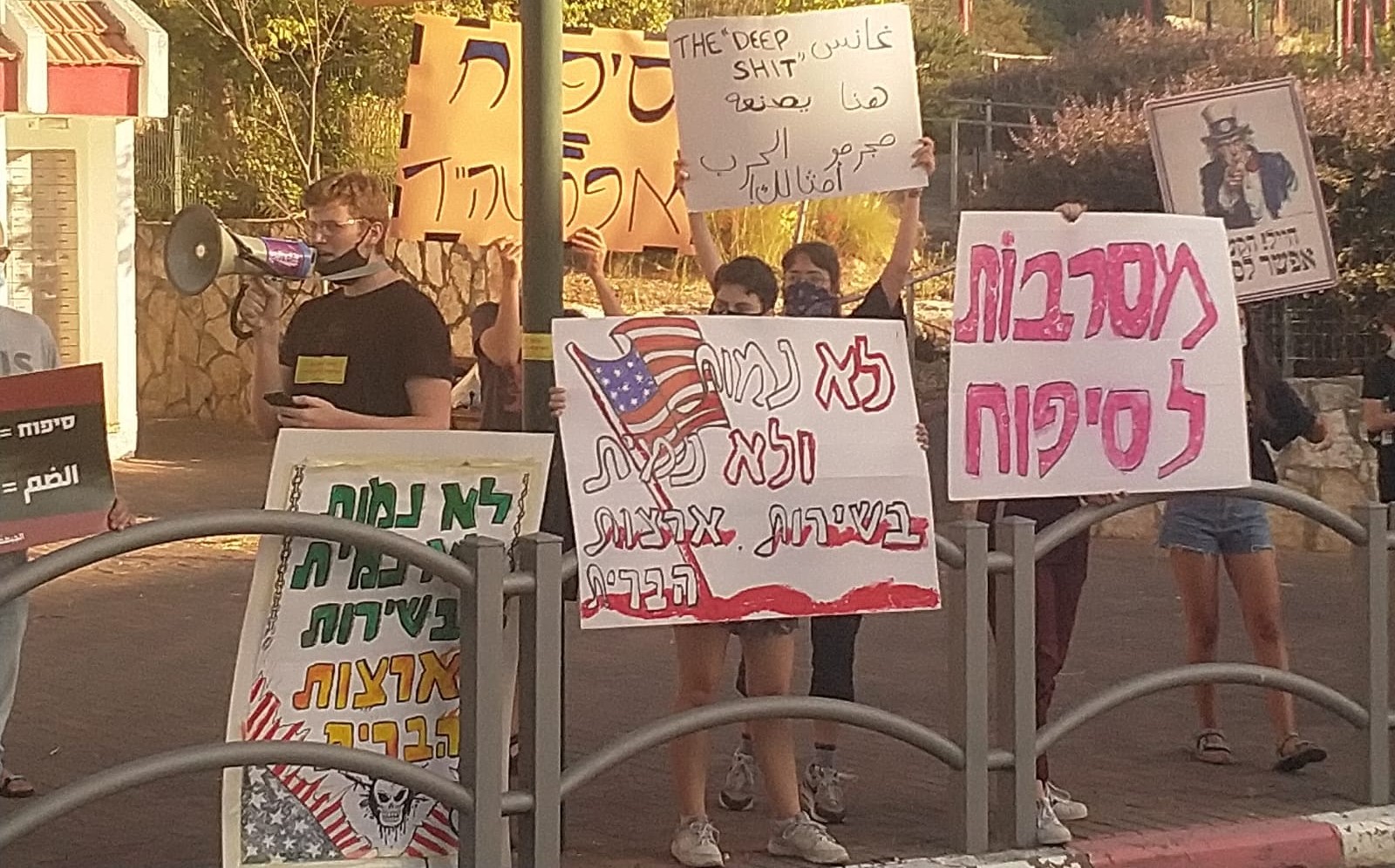 Members of the group "Youth against Annexation" demonstrate near the home of Israel's Minister of Defense, Benny Gantz, in Rosh HaAyin on Thursday, June 25. The placard in Hebrew in the right foreground reads: "Rejecting Annexation." The one with the American flag in the center, like that to the left reads: "We won't die and we won't kill in the service of the United States." The sign in Arabic (and English) held aloft in the center echoes the American profanity Gantz used earlier in the week when referring to the situation the Palestinians have allegedly made for themselves by refusing to enter into a dialog regarding the looming annexation, and reads: "The 'deep s**t' made here by war criminals like you is receding!"