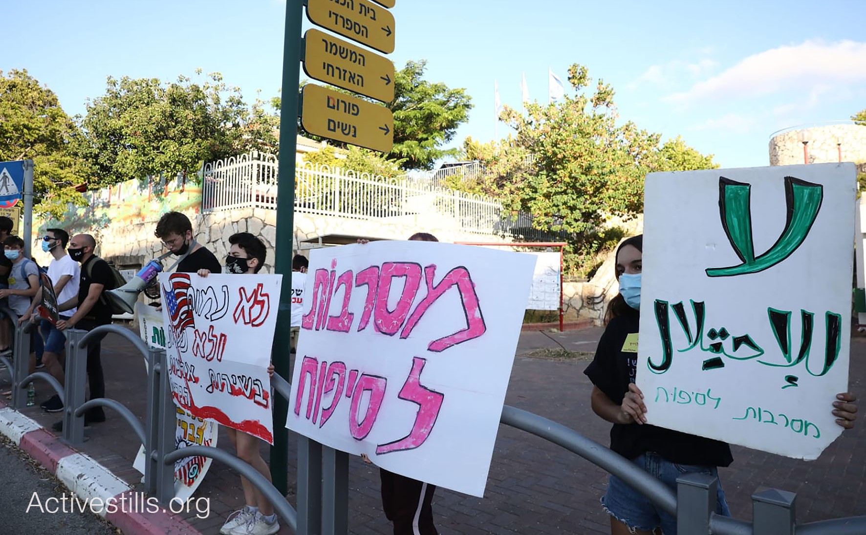 Members of the group "Youth against Annexation" demonstrate near the home of Israel’s Minister of Defense, Benny Gantz, in Rosh HaAyin on Thursday, June 25. The placard at the right reads in Arabic "No to the Occupation" and is signed in Hebrew, "Rejecting Annexation," a slogan repeated in the two-word placard next to it. The sign with the American flag to the left reads in Hebrew: "We won't die and we won't kill in the service of the United States." 
