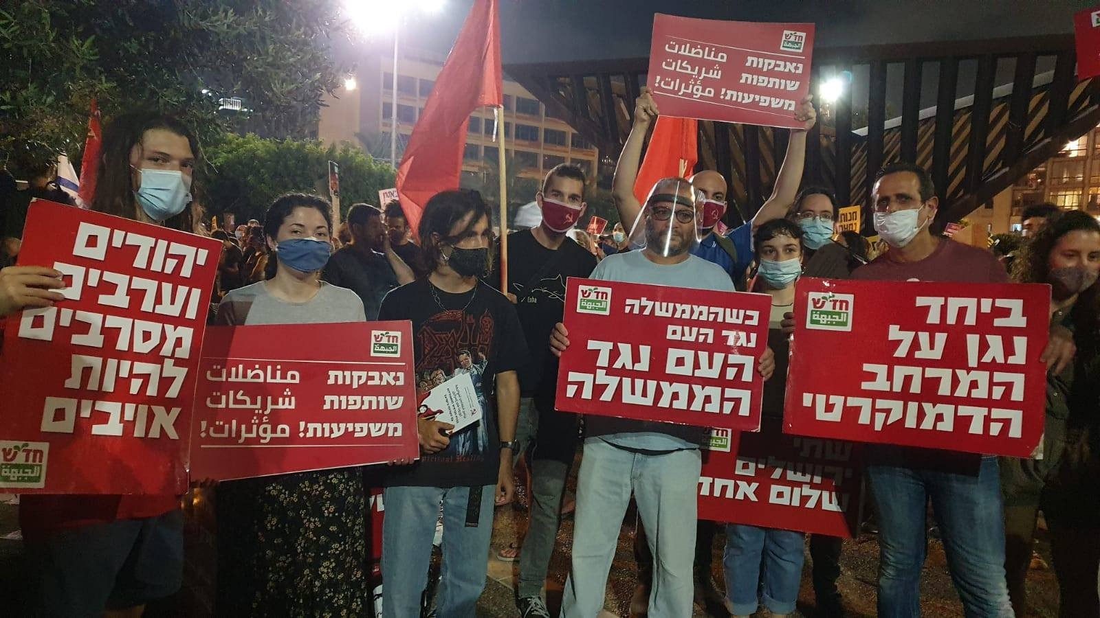 Activists and supporters of Hadash, among them MK Ofer Cassif (fourth from left), demonstrate against the neoliberal handling of the coronavirus economic crisis by Israel's far-right government, Saturday night, July 11, at Rabin Square in Central Tel Aviv. From right to left the Hadash placards read" "Together we'll defend the democratic space"; "When the government is against the people, the people are against the government"; "Struggling, Participating and Influencing"; "Jews and Arabs refuse to be enemies."
