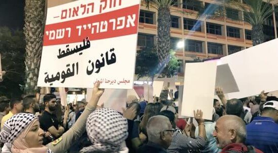 Tens of thousands of protesters demonstrated in Tel Aviv against the "Nation-State Law" in August 2018. The placard held aloft in the foreground reads in Hebrew: "The Nation-State Law – Formal Apartheid”; in Arabic it reads: "Down with the Nation-State Law." 
