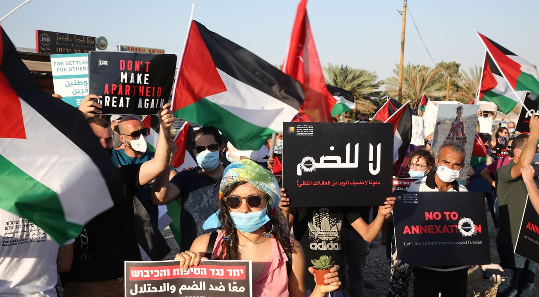 Palestinian and Israeli activists protest against the Israeli occupation and annexation plans at Almog junction, north of the Dead Sea, an area at risk being annexed, June 28, 2020. The dual language sign held in the foreground reads: "Together against the annexation and the occupation."