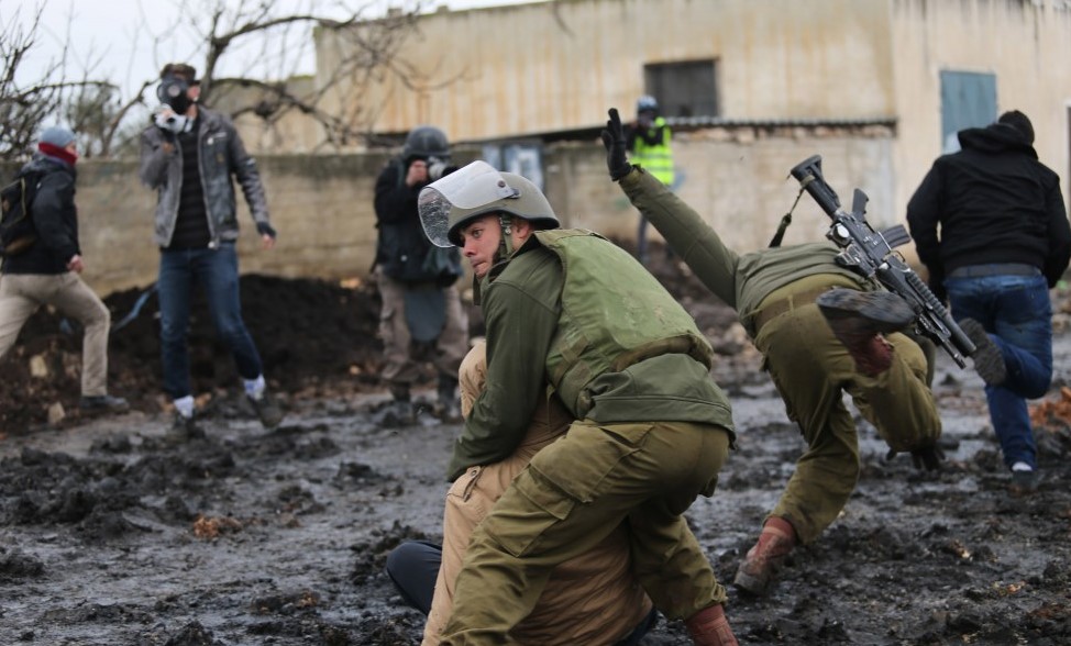 An Israeli soldier slips in the mud as another soldier arrests a Palestinian youth during Kafr Qadum’s weekly protest, January 16, 2015.