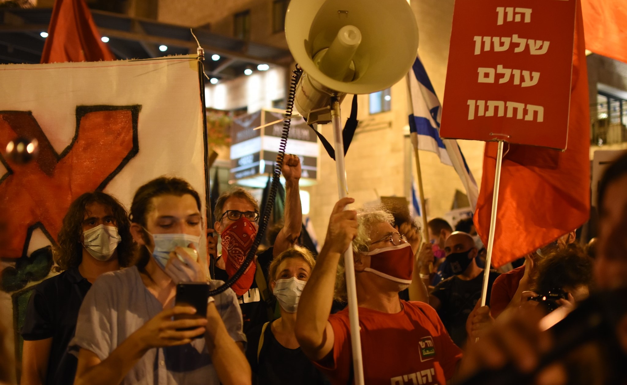 Activists from Hadash and Communist Party of Israel brandish red flags outside far-right Prime Minister Benjamin Netanyahu’s official residence in Jerusalem, Saturday night, September 5. The red sign at the right reads: "[The combination of ] Capital [and] government are an underworld."