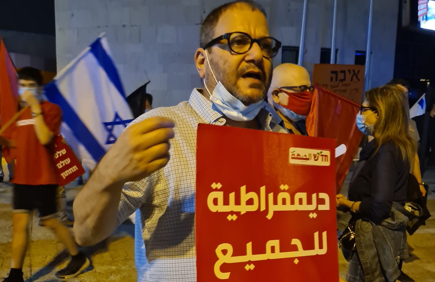 Hadash MK Ofer Cassif (Joint List) at the anti-Netanyahu protest held in Holon, south of Tel Aviv, on Saturday evening, November 7. The Hadash sign reads in Arabic: "Democracy for All."