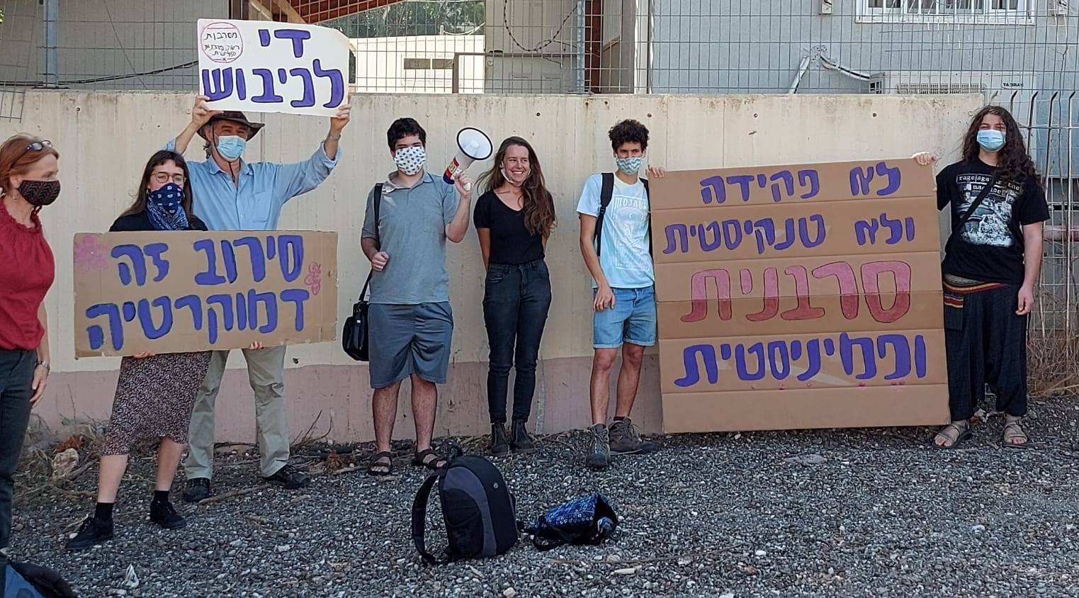 Demonstrators express solidarity with Hallel Rabin (center, wearing black) outside the Tel Hashomer military induction center near Tel Aviv, October 21, 2020. The large placard at the right reads: "Not as a clerk and not in a tank – Rather a refuser and feminist"; at the left the sign held aloft reads "End the occupation"; and the placard below it reads: "Refusal is democracy."