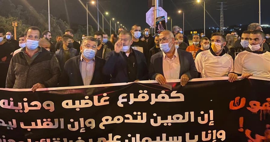 Hundreds march in protest along Route 65 in Wadi Ara following the murder of Sliman Naziye Masarweh, 25, a resident of the town, Wednesday, January 6, 2021. Hadash MK Youssef Jabareen, second from left, was among the protestors. In part, the banner reads: "Kafr Qara is angry and saddened; our eyes are full of tears and our hearts [illegible]… and that, O Sliman, … [illegible]"