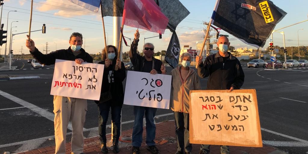 Demonstrators protest against Netanyahu at an intersection near Haifa, Saturday, January 16, 2021. From left to right the signs read: "The vaccine doesn't cure corruption," "Political lockdown," and "You're in lockdown so that he can suspend the trial."