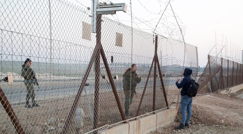 Two Israeli women soldiers stop a Palestinian worker as he tries to cross to his place of work in Israel through a hole in the fence near the city of Qalqilya, occupied West Bank, January 10, 2021.