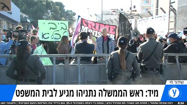 Protesters call for Prime Minister Benjamin Netanyahu's resignation on Monday, February 8, outside the Jerusalem courthouse where his trial is about to resume. The caption beneath the live broadcast image reads: "Prime Minister Netanyahu is about to arrive at court."