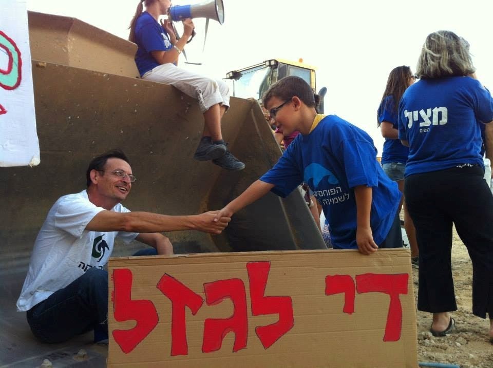 Dov Khenin attends a demonstration against construction on the Palmahim beach along Israel's southern Mediterranean coast. The sign held by the boy reads "Enough Robbery."