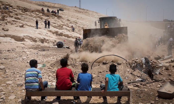 Children from the Palestinian Bedouin village of Khan al-Ahmar look on as a bulldozer makes preparations for an access road to be used by Israeli forces in the "imminent evacuation and demolition" of the West Bank hamlet, July 4, 2018.