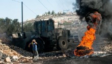A demonstrator hurls a stone at an Israeli army bulldozer during the weekly demonstration against the occupation in the West Bank village of Kafr Qaddum, October 25, 2013.