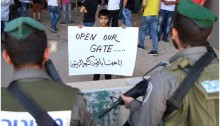 Palestinians from the West Bank village of Al Zaeem call for the opening of the Separation Wall gate that leads from Jerusalem to their village, May 8, 2015. The Arabic slogan in the sign held by the boy confronting the soldiers reads: “I will remain here like an olive tree.”