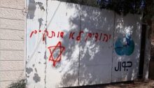 A threat spray-painted in red "Jews don't remain silent" defaces the entrance gate to a building in the occupied West Bank town of Yatma, 15km south of Nablus, August 13, 2019. The building serves as offices to Jawwal, identified by its logo to the right, a major Palestinian-owned cellular communications company.