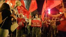 Joint List MK Ofer Cassif (Hadash, center) and activists from Hadash and Communist Party of Israel brand red flags outside far-right Prime Minister Benjamin Netanyahu's official residence in Jerusalem, Saturday night, August 29. The placard Cassif is holding reads: "Salaried workers, independents and unemployed together against the government."